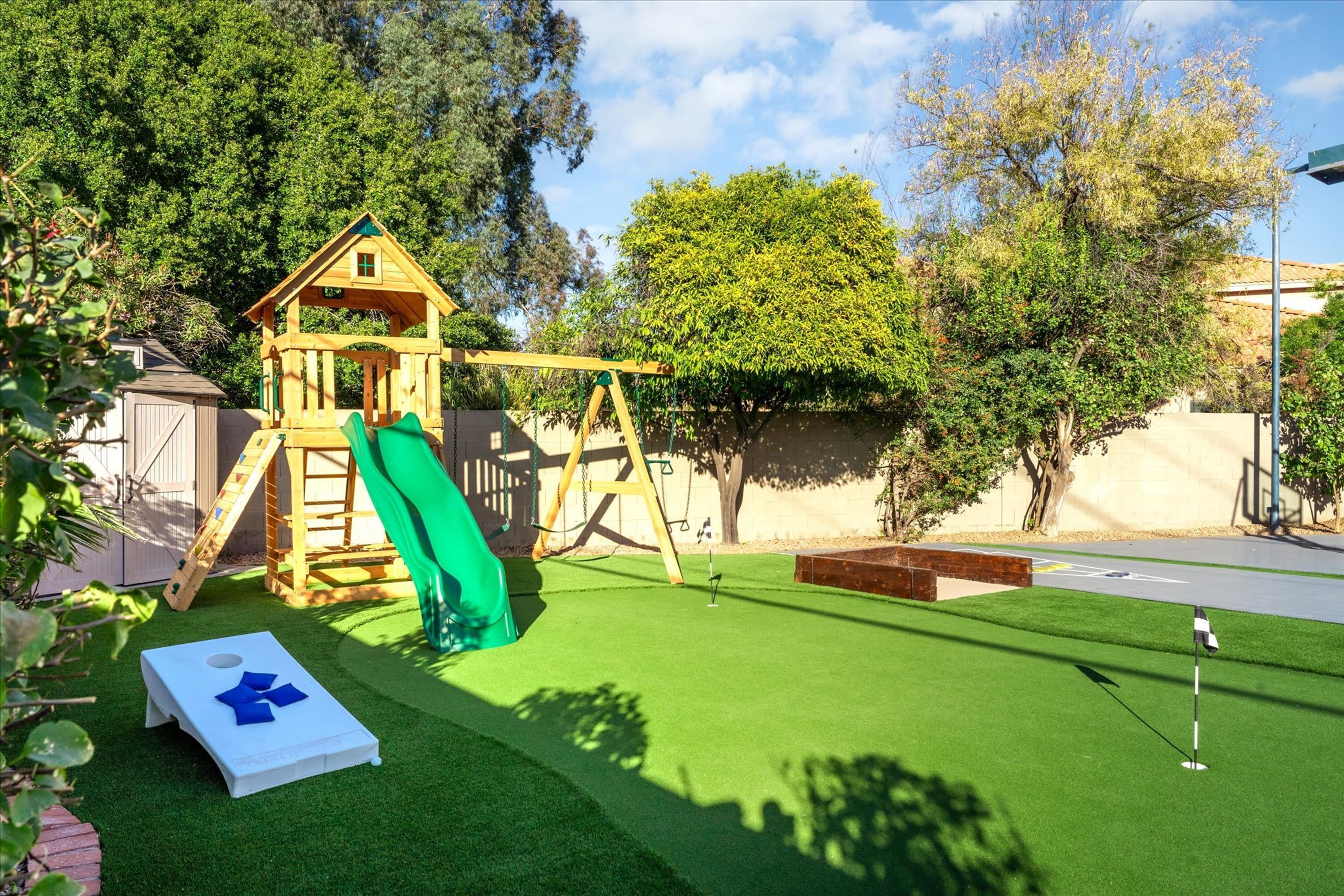 Une cabane en bois pour enfants, avec un toboggan, une balançoire et une pelouse artificielle.