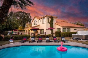 A pool area with lounge chairs and a hot tub, surrounded by a building with a tiled roof.