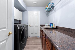 A laundry room with a front-loading washer and dryer, a white door, and a countertop with cleaning supplies.