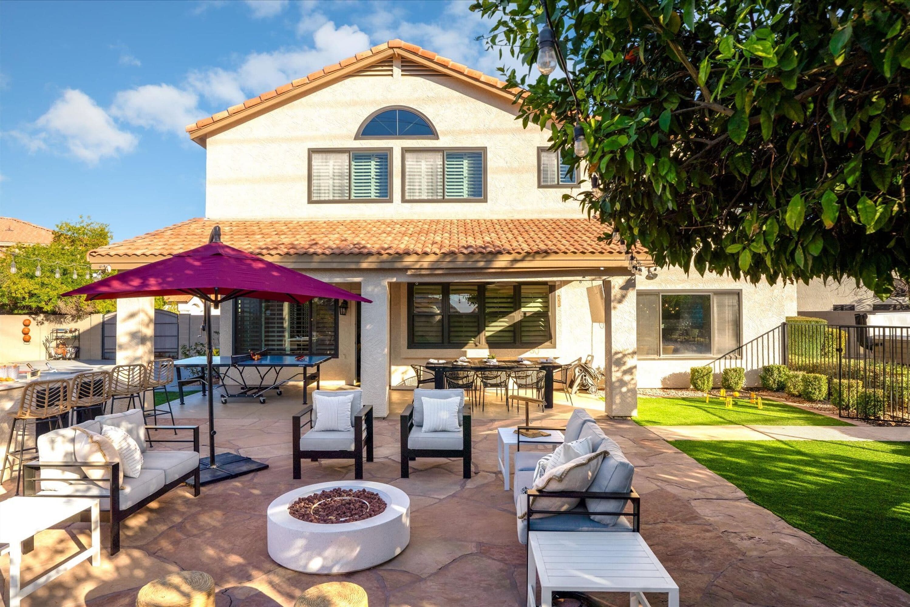 A two-story house with a patio area featuring outdoor furniture, a fire pit, and a pergola with string lights.