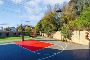 A basketball court with a red playing surface, a basketball hoop, and a playground with a slide. - Epic Family Getaway Sport Court Heated Pool (Scottsdale)