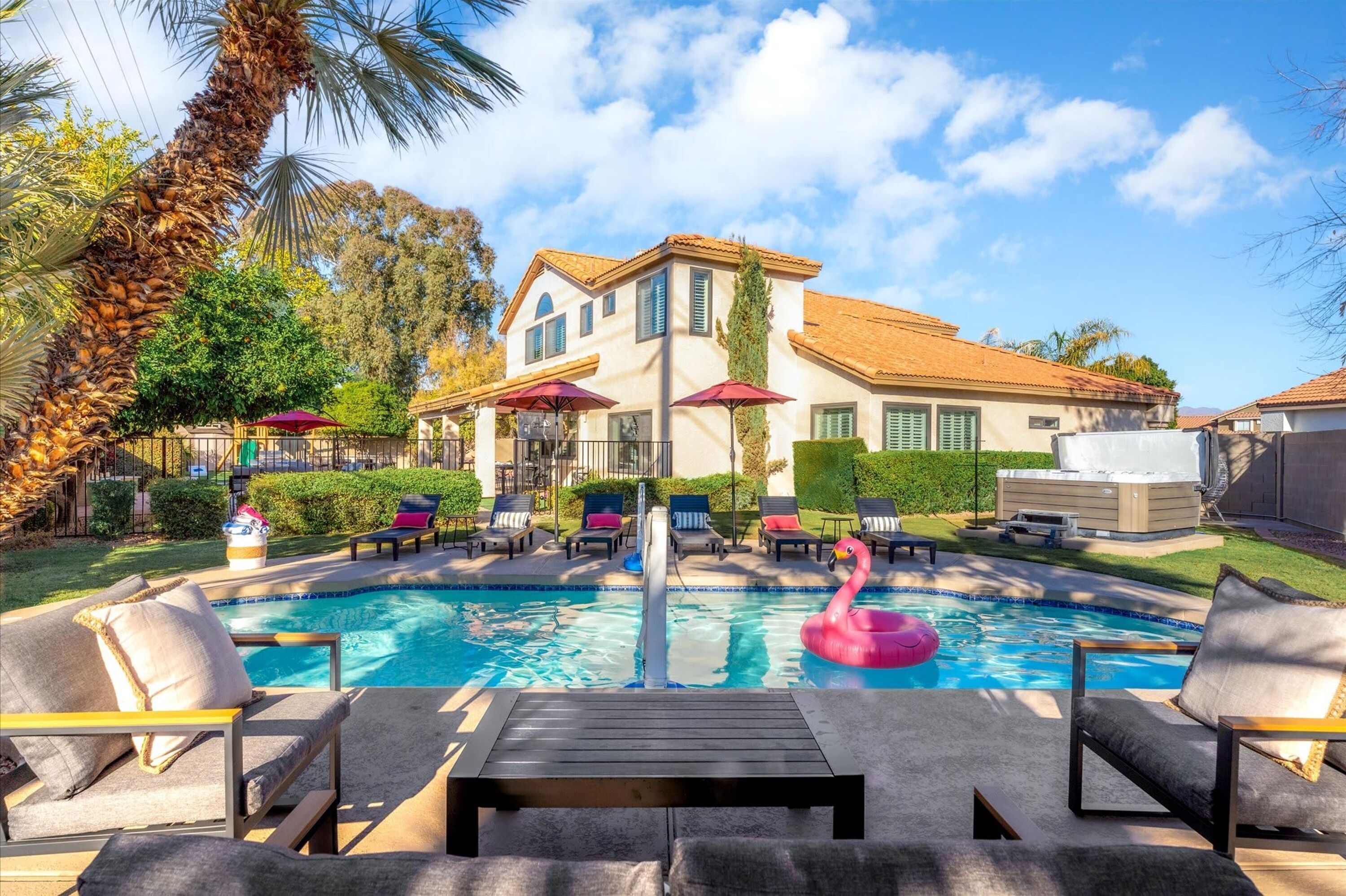 A pool area with lounge chairs, a flamingo float, and a building with a tiled roof.