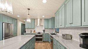 Una cocina moderna con gabinetes color turquesa, electrodomésticos de acero inoxidable y encimera de mármol.