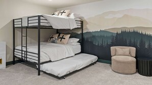 Una cama litera con un mural de montaña al fondo, una silla redonda y una pequeña mesa.