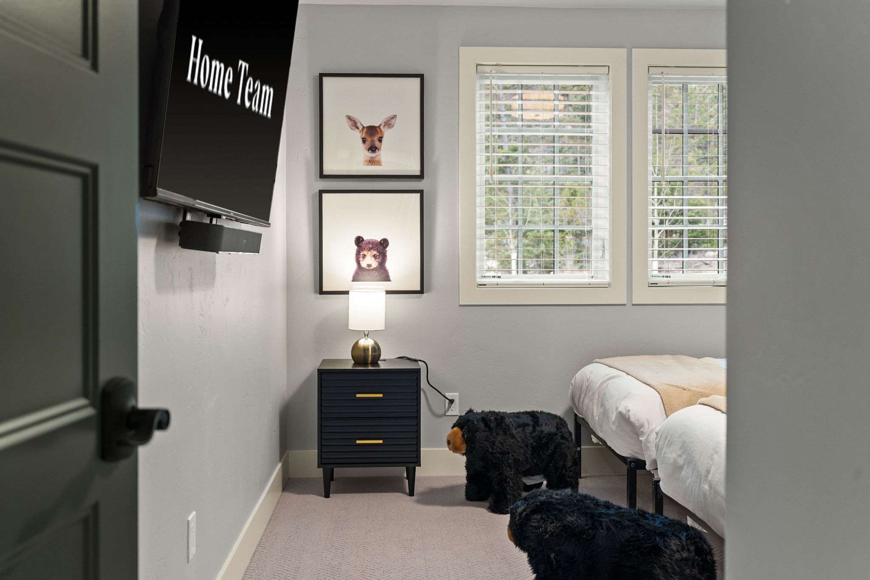 A bedroom with a bed, a nightstand with a lamp, a wall-mounted TV, and two framed animal pictures.