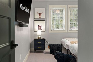 Quarto com cama, mesa de cabeceira com abajur, televisão fixada na parede e duas fotos emolduradas de animais.