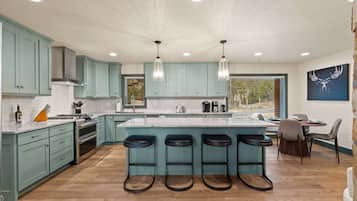 A modern kitchen with teal cabinets, a large island with bar stools, and a dining area with a table and chairs.