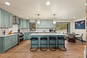 Uma cozinha moderna com armários verde-água, uma ilha grande com banquetas e uma área de jantar com mesa e cadeiras.