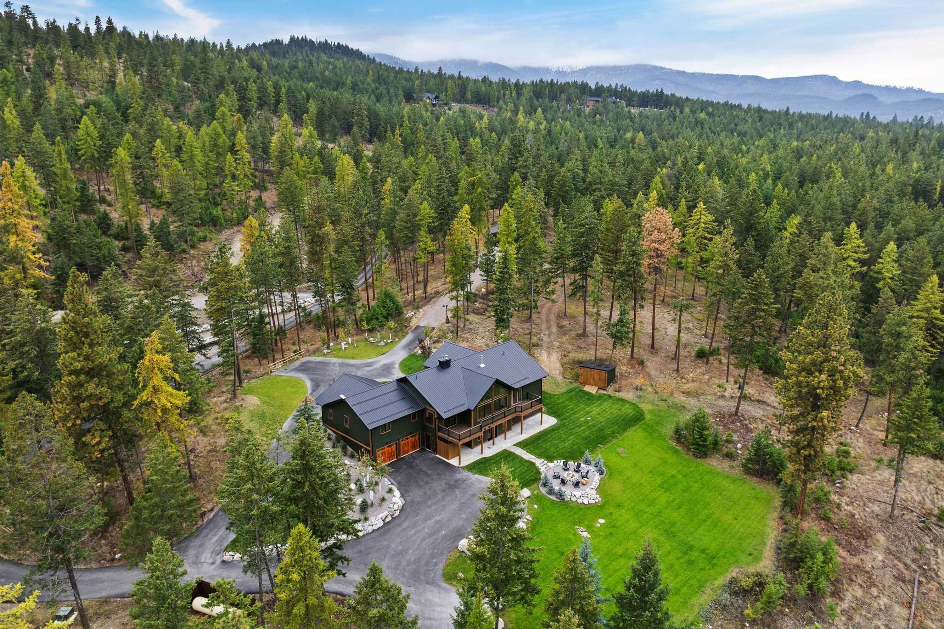 A large, modern house with a spacious deck and a well-maintained lawn, surrounded by dense forest.
