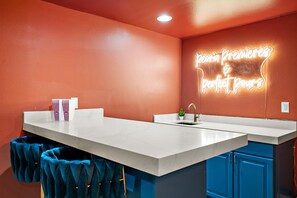 A modern kitchen with a neon sign, a marble countertop, and blue cabinets. - AZ Game House Sport Court - Golf - Pool - Games (Peoria)