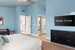 A bedroom with a bed, a dresser, a ceiling fan, and a door leading to another room. - AZ Game House Sport Court - Golf - Pool - Games (Peoria)