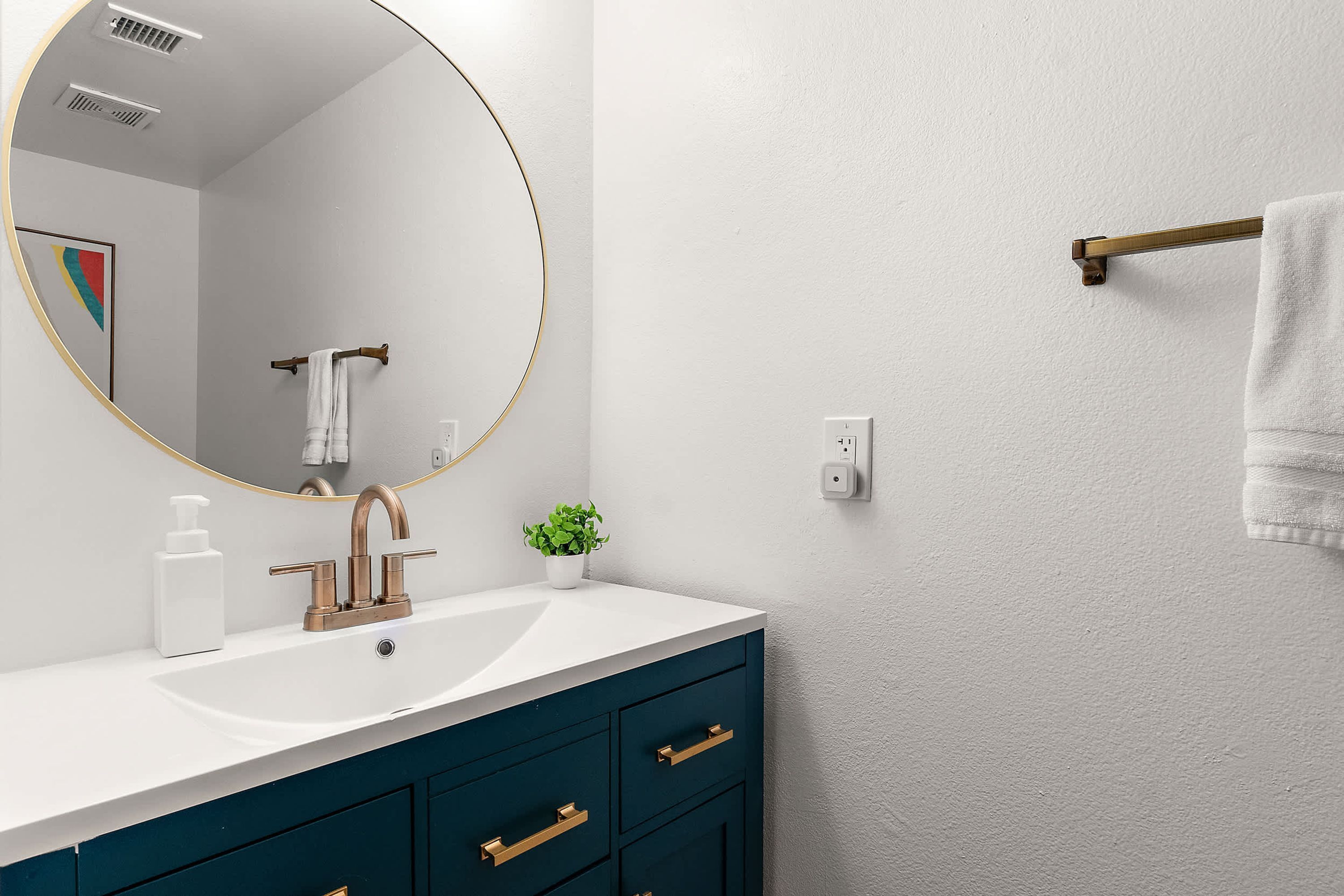 A bathroom with a round mirror, a white sink, a small potted plant, and a towel rack.