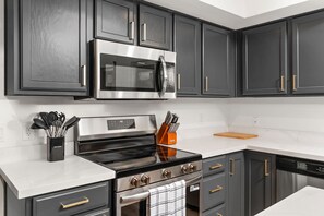 A modern kitchen with dark cabinetry, stainless steel appliances, and a white countertop. - AZ Game House Sport Court - Golf - Pool - Games (Peoria)