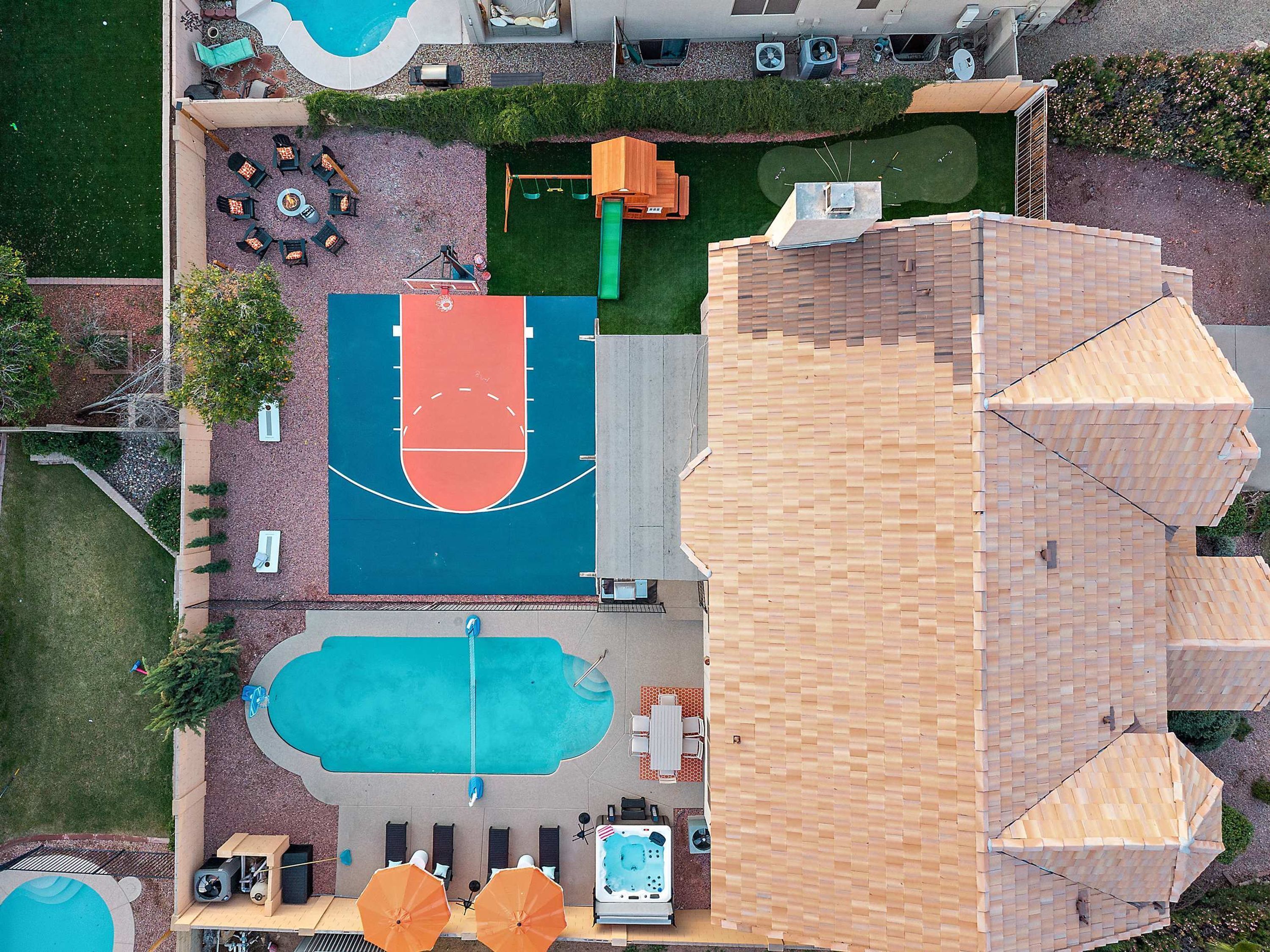 Vista aérea de una propiedad con cancha de baloncesto, piscina, asientos al aire libre y un patio cubierto.