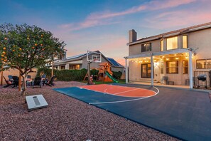 Ein Basketballplatz mit Rutsche, umgeben von Kiesflächen und einem Baum mit Früchten.