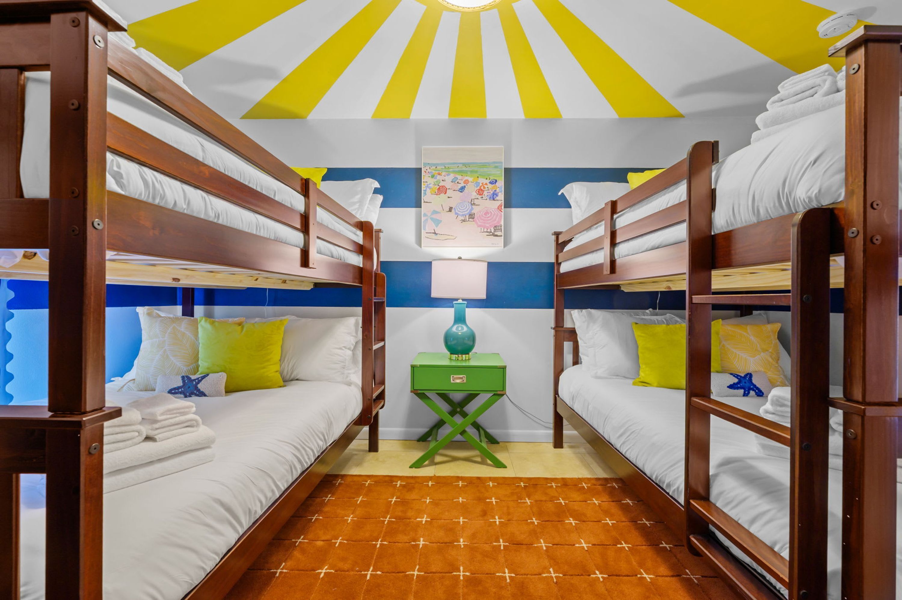 Ein Zimmer mit Etagenbetten, einem grünen Nachttisch und einer Wanddekoration zum Thema Strand.