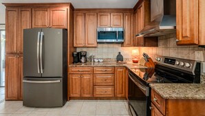 A kitchen with wooden cabinets, a stainless steel refrigerator, a microwave, a coffee maker, and a stove. - Basketball Pickleball Pool Movie Game Room (Largo)