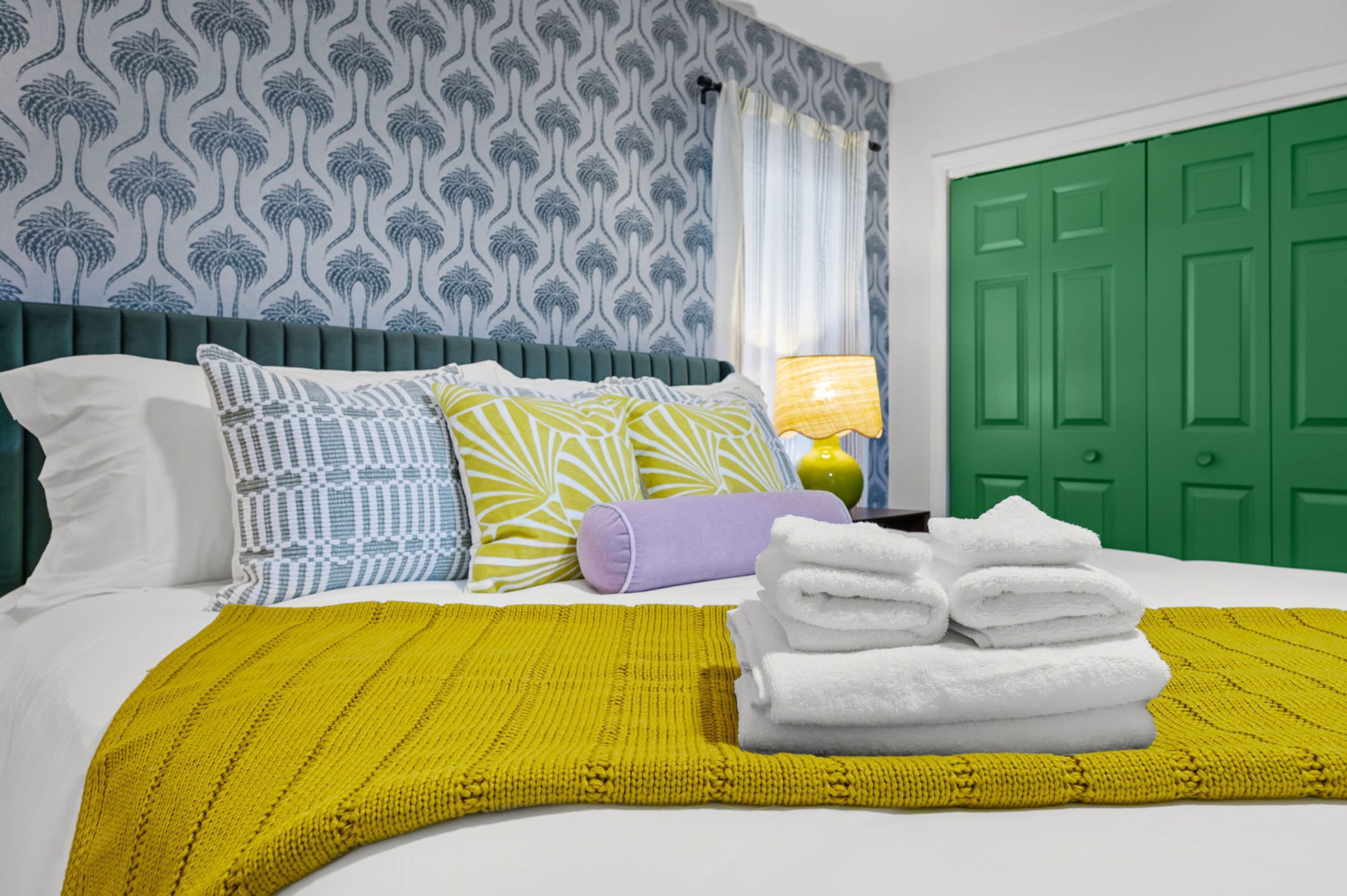 A neatly made bed with pillows, a yellow throw blanket, and a stack of white towels.