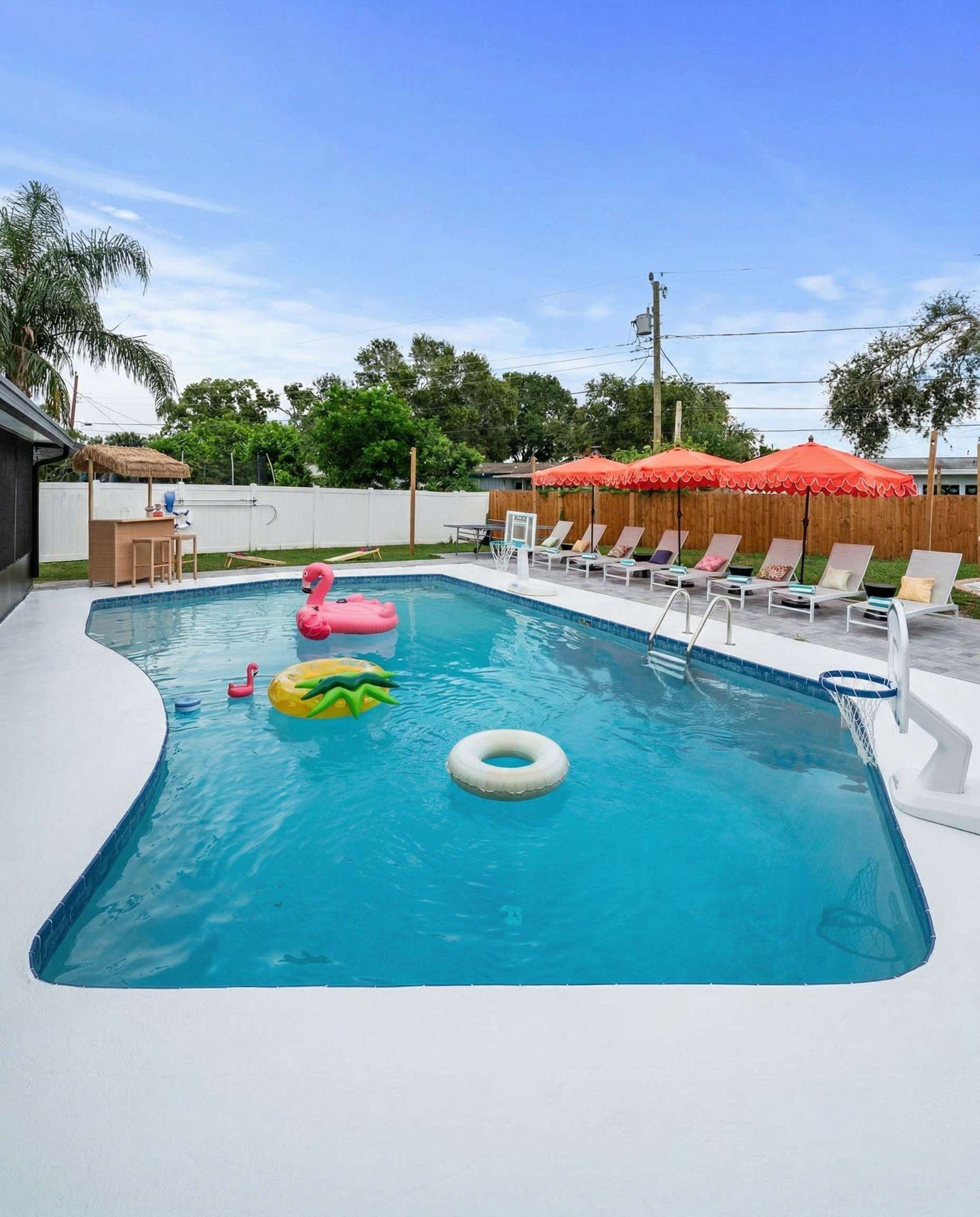 A swimming pool with lounge chairs and a wooden fence in the background.