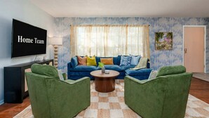 A living room with a blue sofa, green armchairs, a coffee table, and a TV on the wall. - Basketball Pickleball Pool Movie Game Room (Largo)