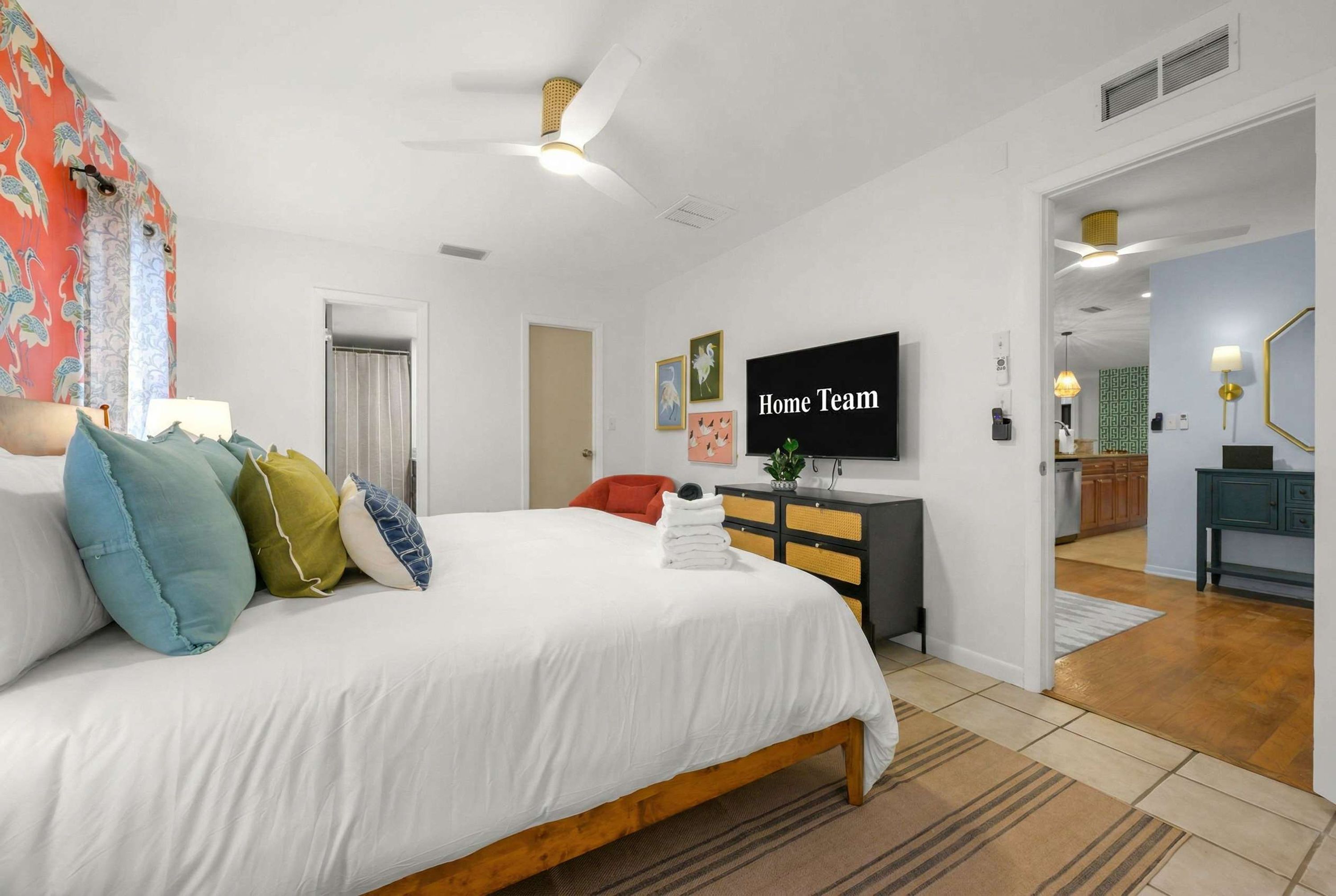 A bedroom with a bed, pillows, a TV, a dresser, and a bathroom visible in the background.