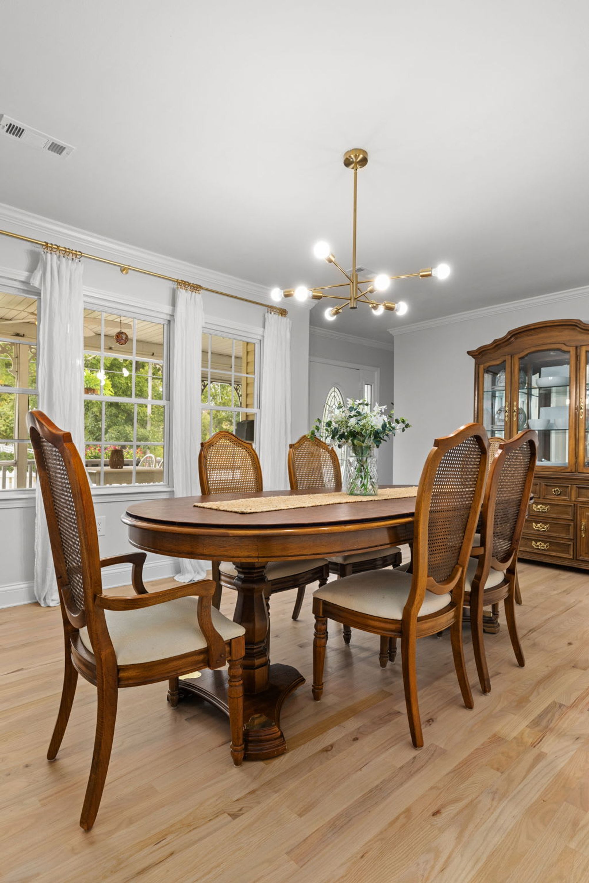 A dining room with a wooden table and chairs, a chandelier, and a large window with curtains.