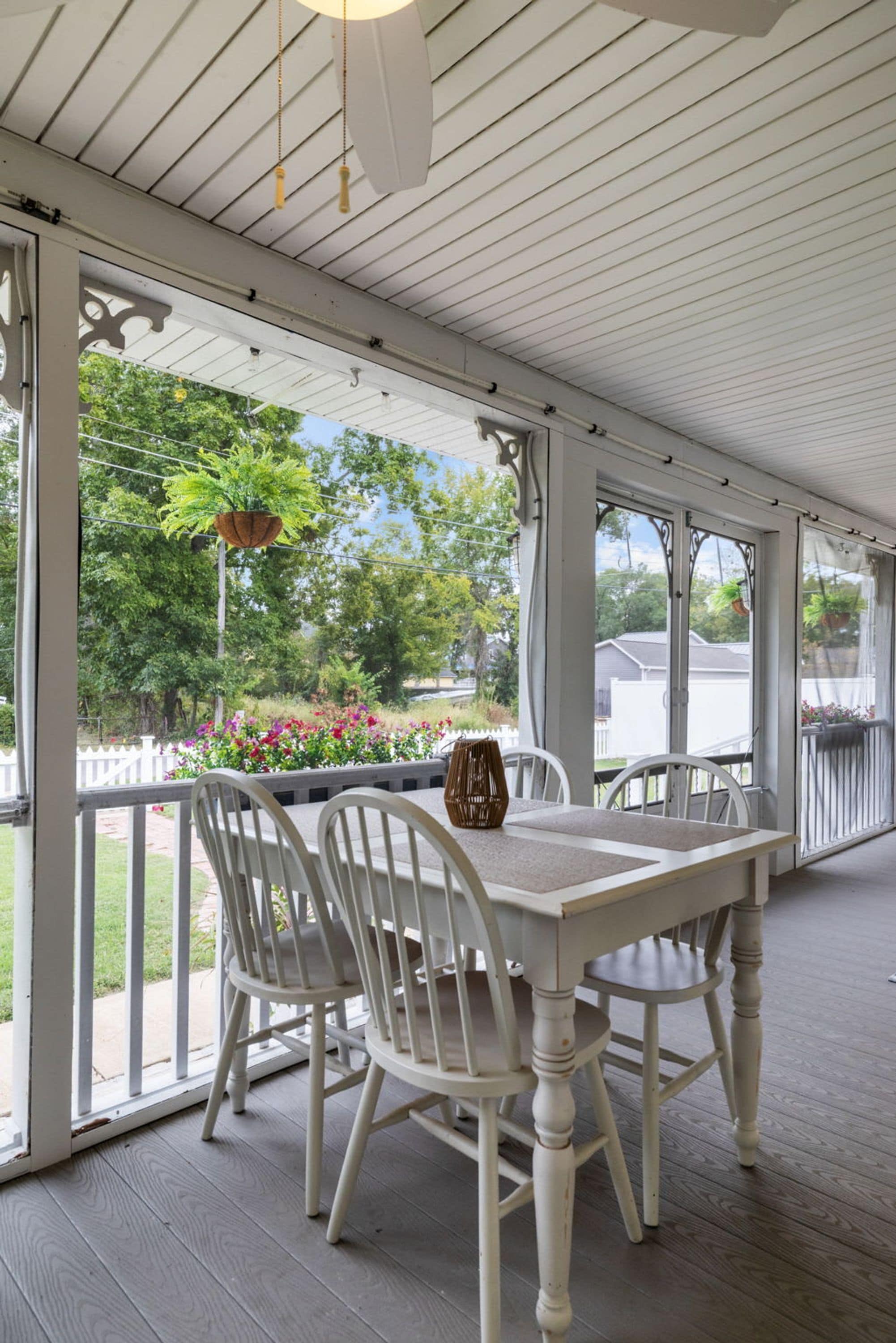 A covered patio with a table and chairs, a hanging plant, and a view of a garden.