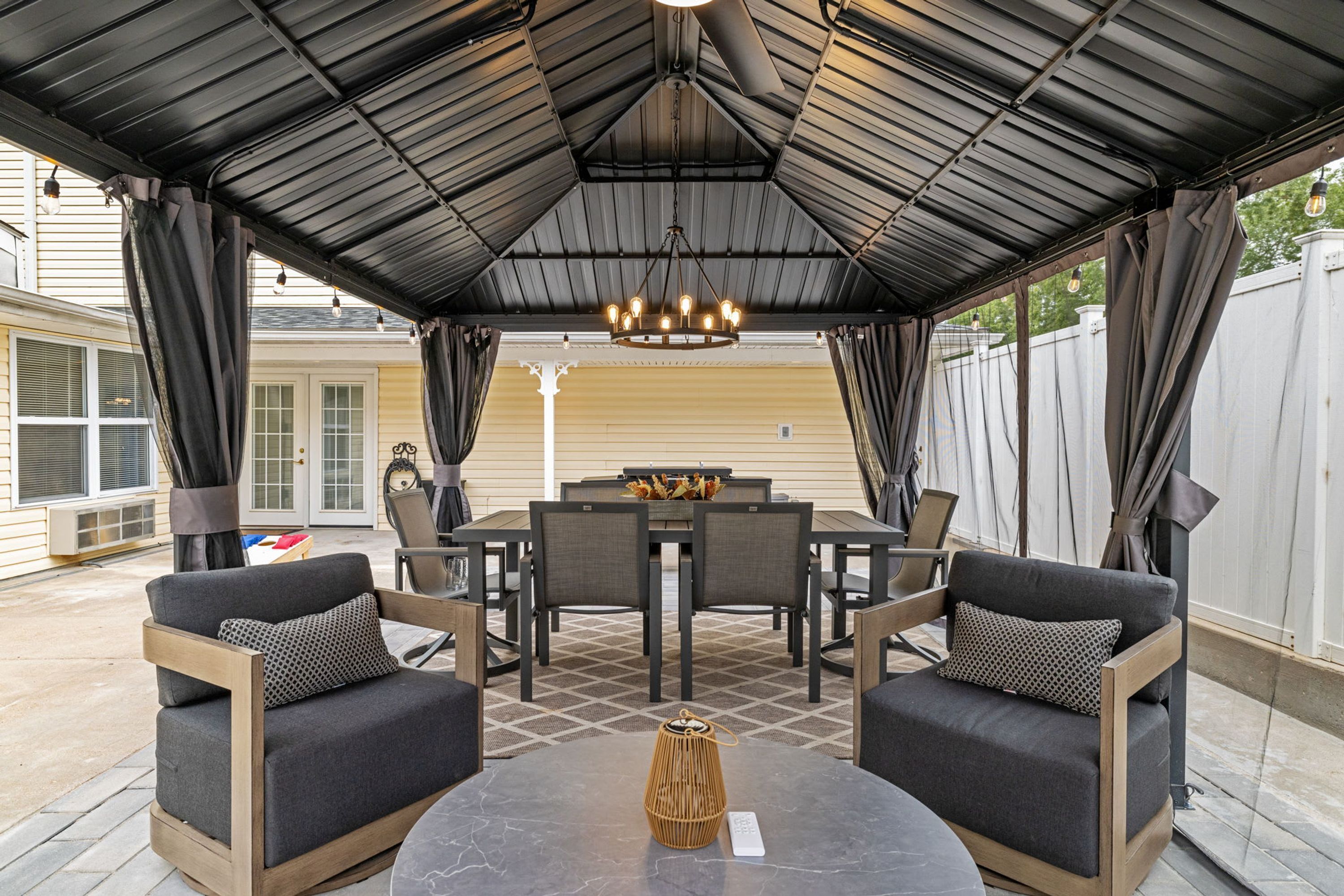 An outdoor patio with a covered seating area, a dining table, and a chandelier.
