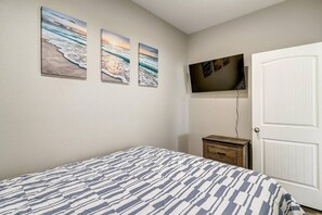 Une chambre à coucher comprenant un lit, une commode, un téléviseur fixé au mur et trois tableaux encadrés.