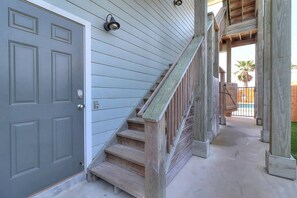 A wooden staircase leading to a covered outdoor area with a pool. - Nauti Paradise- Private Pool Game Room (Port Aransas)