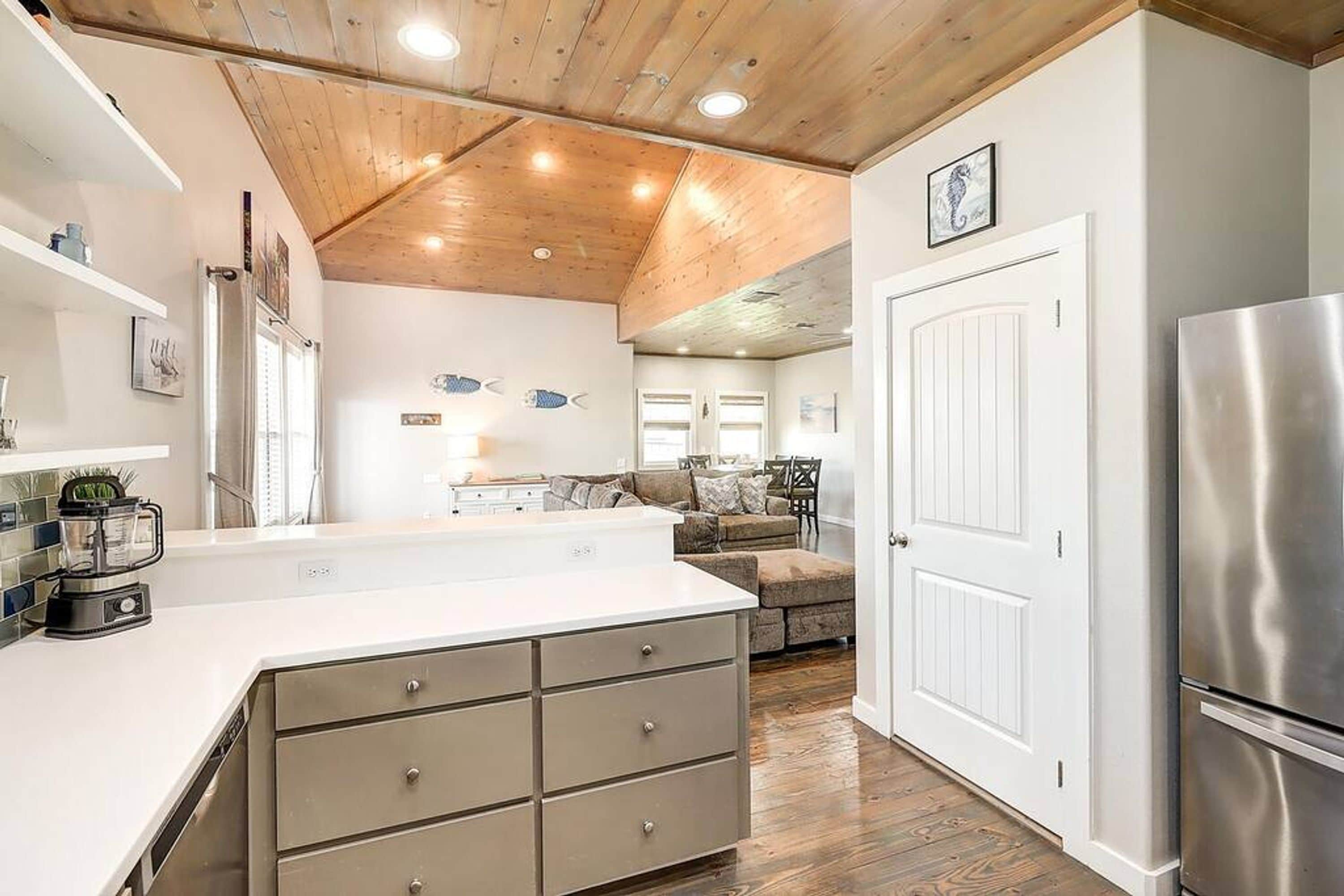 A kitchen with a wooden ceiling, a white refrigerator, and a dining area with a couch and table.