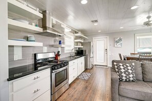 A modern kitchen with white cabinetry, a black stove, and a microwave. There is a wooden floor and a gray sofa with a patterned pillow. - Nauti Paradise- Private Pool Game Room (Port Aransas)