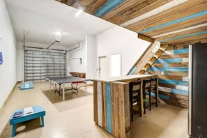 Une pièce avec une table de ping-pong, une petite table bleue et un escalier avec des panneaux de bois.
