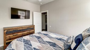 Ein Schlafzimmer mit einem Bett, einer hölzernen Kommode, einem Deckenventilator, einem Fernseher und einer Tür zu einem anderen Raum.