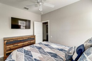 A bedroom with a bed, a wooden dresser, a ceiling fan, a television, and a door leading to another room. - Nauti Paradise- Private Pool Game Room (Port Aransas)