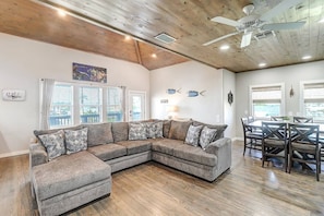 A modern living room with a sectional sofa, dining area, and a ceiling fan. - Nauti Paradise- Private Pool Game Room (Port Aransas)