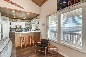 A kitchen with a central island, bar stools, a black chair, and a wicker basket. - Nauti Paradise- Private Pool Game Room (Port Aransas)
