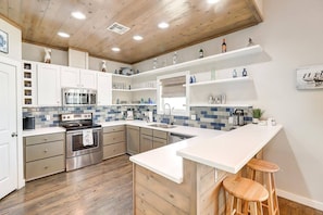 A modern kitchen with a central island, stainless steel appliances, and blue-tiled backsplash. - Nauti Paradise- Private Pool Game Room (Port Aransas)