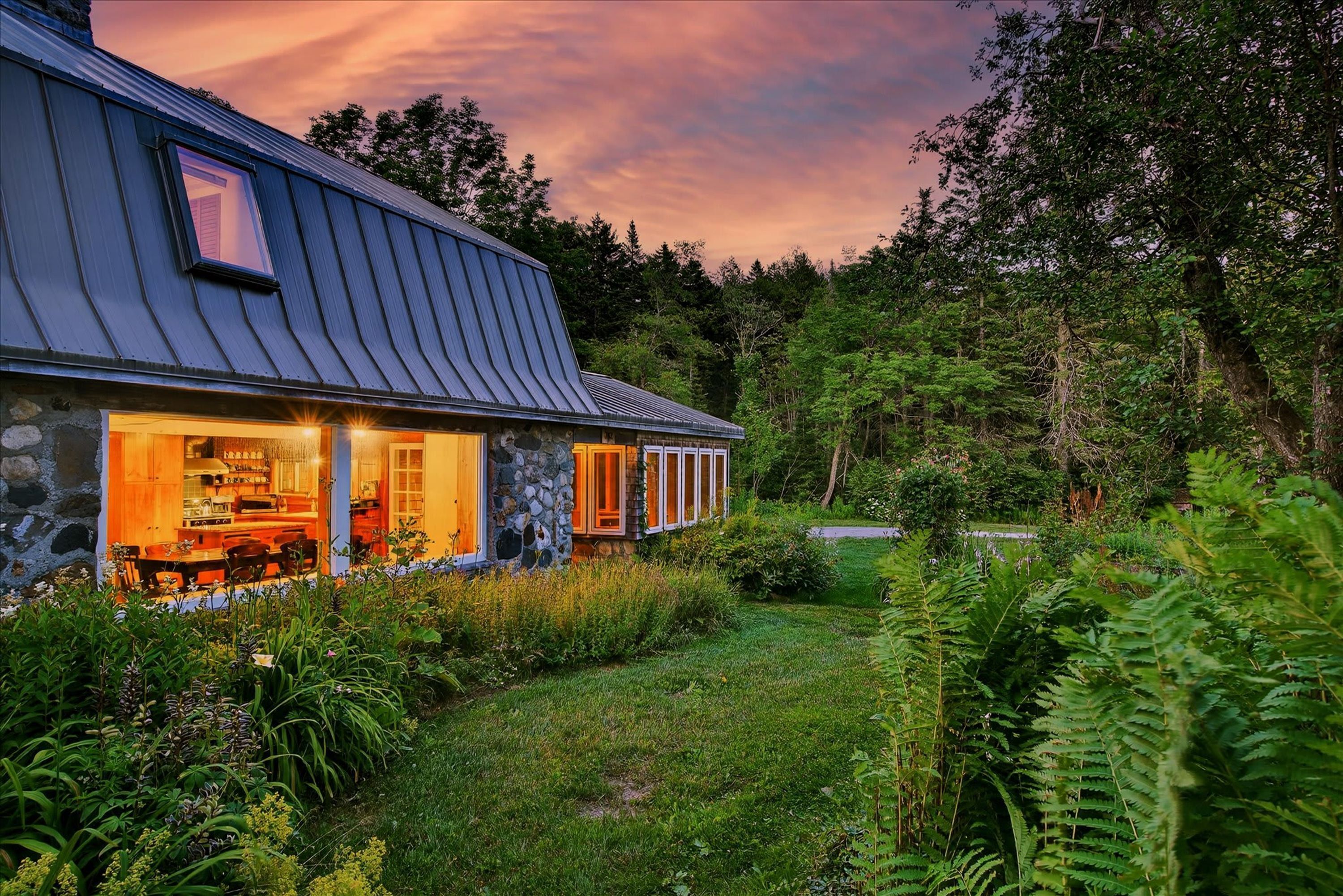 A rustic stone building with a sloped metal roof, a dining area with wooden furniture, and a stone exterior wall.