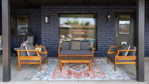 A covered outdoor seating area with two wooden chairs and a sofa, a patterned rug, and a glass door leading to a pool. - Sport Court Private Heated Pool Mini Golf More (Glendale)