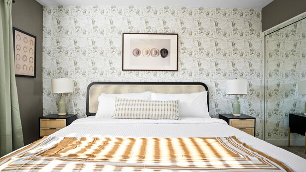 A bedroom with a bed, two bedside tables, a framed picture, and patterned wallpaper. - Sport Court Private Heated Pool Mini Golf More (Glendale)