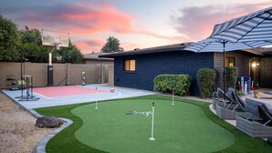 A backyard with a basketball court, a putting green, and a patio area with outdoor furniture. - Sport Court Private Heated Pool Mini Golf More (Glendale)