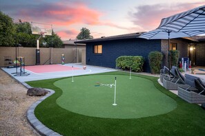 Ein Garten mit Basketballplatz, Putting-Green und einer Terrasse mit Gartenmöbeln.