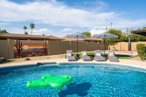 Ein Swimmingpool mit Liegestühlen und Sonnenschirmen, ein Wandgemälde und ein Basketballkorb.