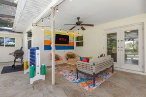 A covered outdoor area with a ceiling fan, a television screen displaying 'NETFLIX,' and a colorful rug. - Pool Games More Fun for Everyone (Palm Harbor)