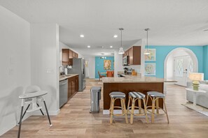 A modern kitchen with a central island, bar stools, and a dining area with a white table and chairs. - Pool Games More Fun for Everyone (Palm Harbor)