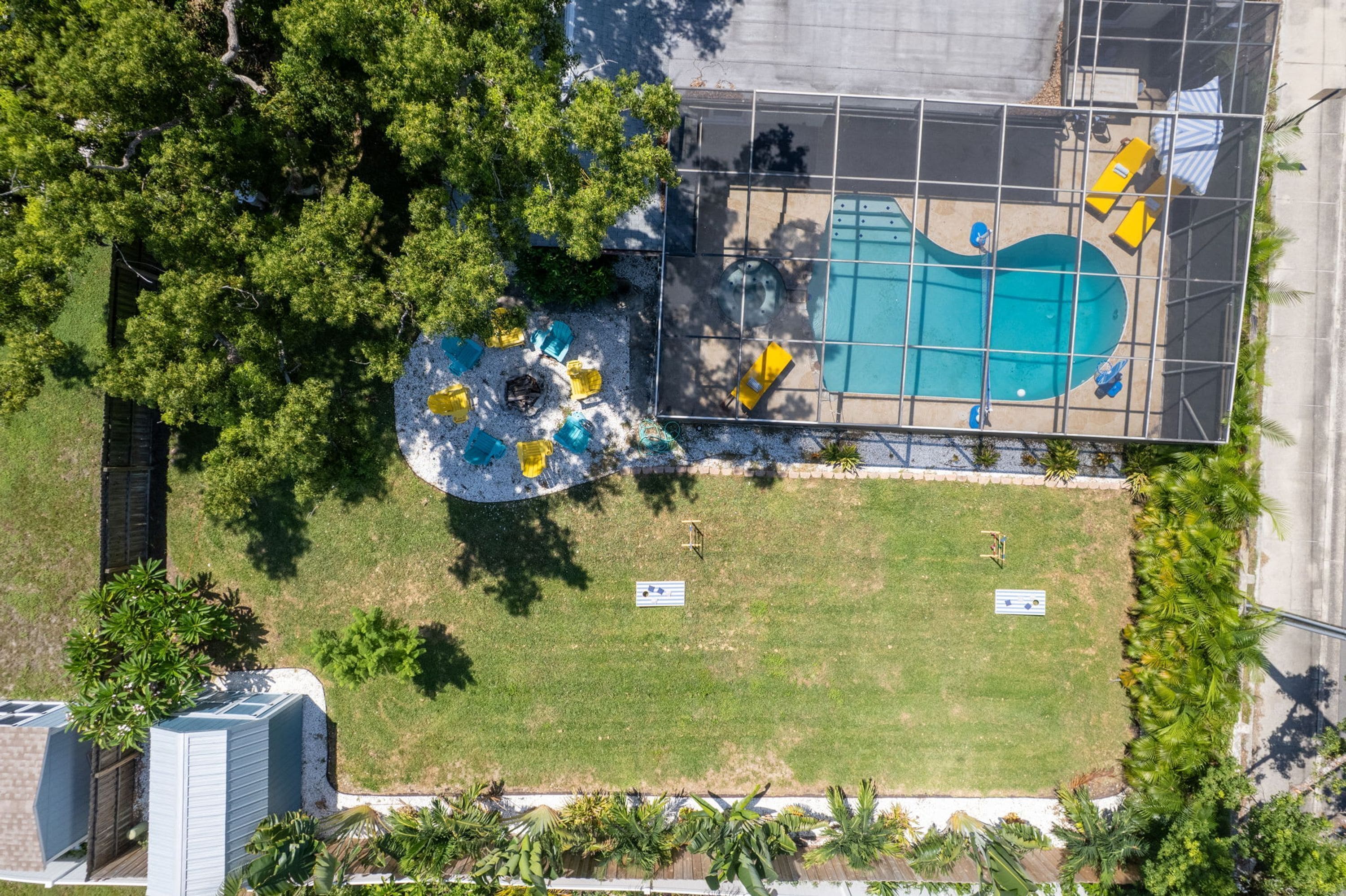 An aerial view of a swimming pool area with a fenced deck, surrounded by trees and grass.