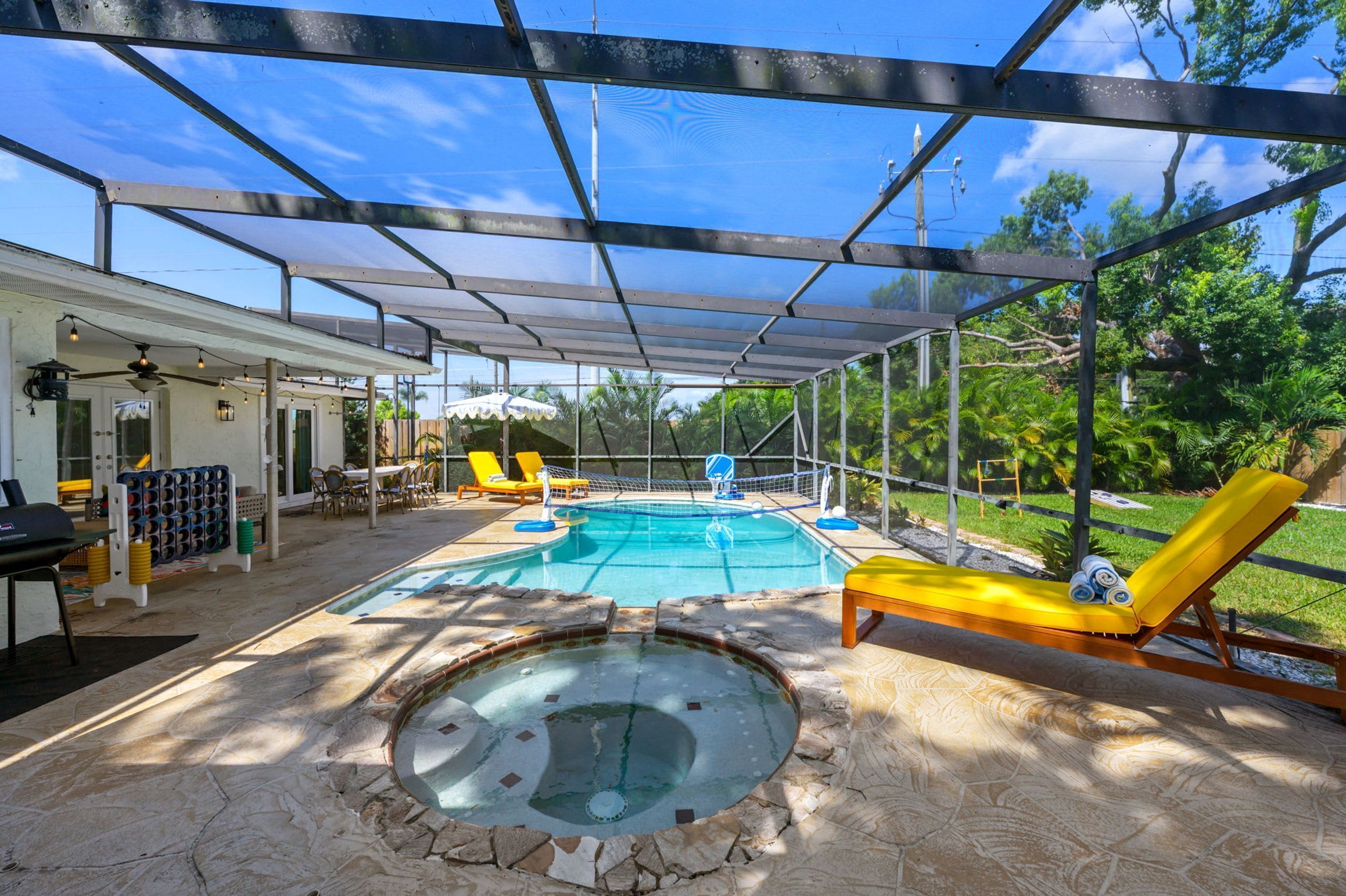 An outdoor swimming pool area with a covered patio, lounge chairs, and a hot tub.