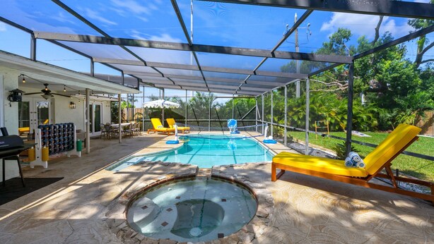 Ein Außenpoolbereich mit überdachter Terrasse, Liegestühlen und einem Whirlpool.