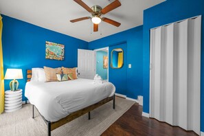 A bedroom with a bed, a ceiling fan, a painting, a mirror, and a door. - Pool Games More Fun for Everyone (Palm Harbor)